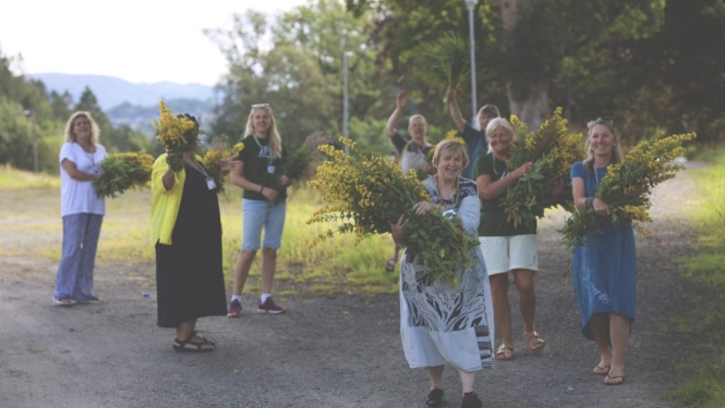 Vidzemes reģiona remigrācijas koordinatore Inga Madžule kopā ar remigrantiem rokās nes lielus dzeltenu ziedu klēpjus.