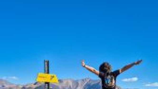 Remigrante Krista Nevis lēcienā no mugurpuses klinšaina kalna galotnē ar virziena rādītājiem.