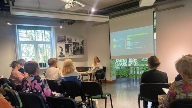 Cēsu Centrālās bibliotēkas telpa ar prezentāciju ekrānu un klausītājiem - Vidzemes bilbiotekāriem.