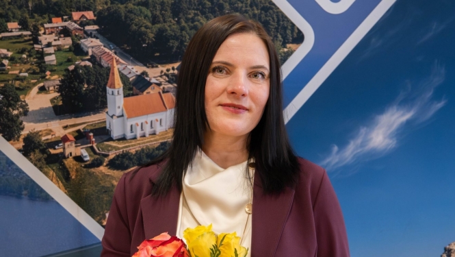 A young woman with dark brown hair stands holding yellow and pink roses, with a church visible in the background.