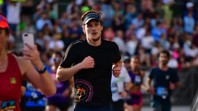 Edgars Prūsis skrien maratonā Maiami, finiša posmā starp citiem skrējējiem, simbolizējot aktīvu dzīvesveidu un atgriešanās ceļu mājās..
