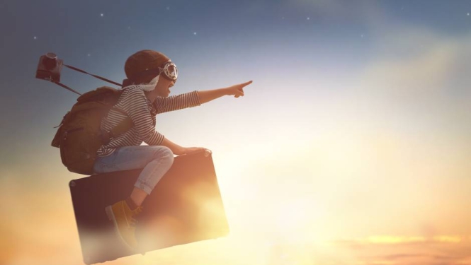 Cilvēks aviatora cepurē un brillēs ar mugursomu plecos lido uz ceļojumu kofera saulrieta debesu fonā un ar izstieptu rādītājpirkstu rāda uz priekšu.