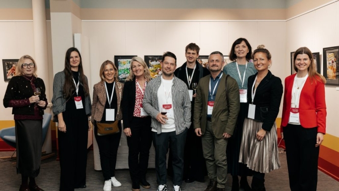Desmit pasākuma "Biznesa diena Parīzē 2025" dalībnieki ar gleznām fonā.