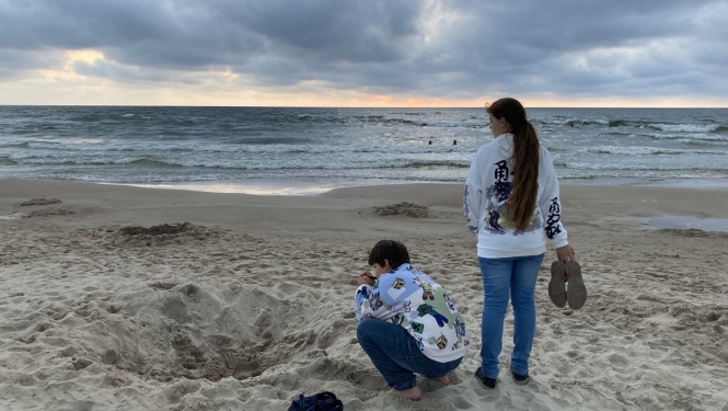 Meitene un zēns atrodas jūras krastā pievakarē, zēns spēlējas ar smiltīm, bet meitene raugās tālumā