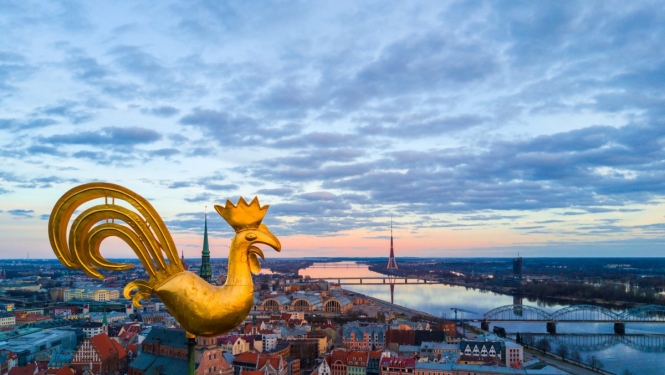 Rīgas panorāmas skats, kur attēlots baznīcas zelta gailis un teksts “Atgriezies Rīgā un reģionā: Rīga, Jūrmala + Ādažu, Salaspils, Siguldas, Mārupes, Olaines, Ķekavas, Ropažu novads".