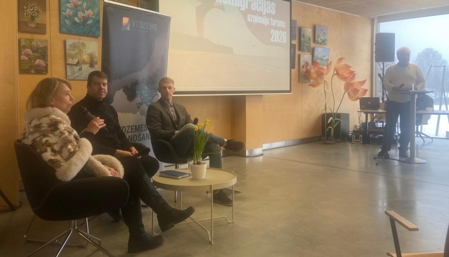 Remigrācijas uzņēmēju forums Ungurpilī – diskusija ar runātājiem, fonā prezentācijas ekrāns un Vidzemes plānošanas reģiona simbolika.