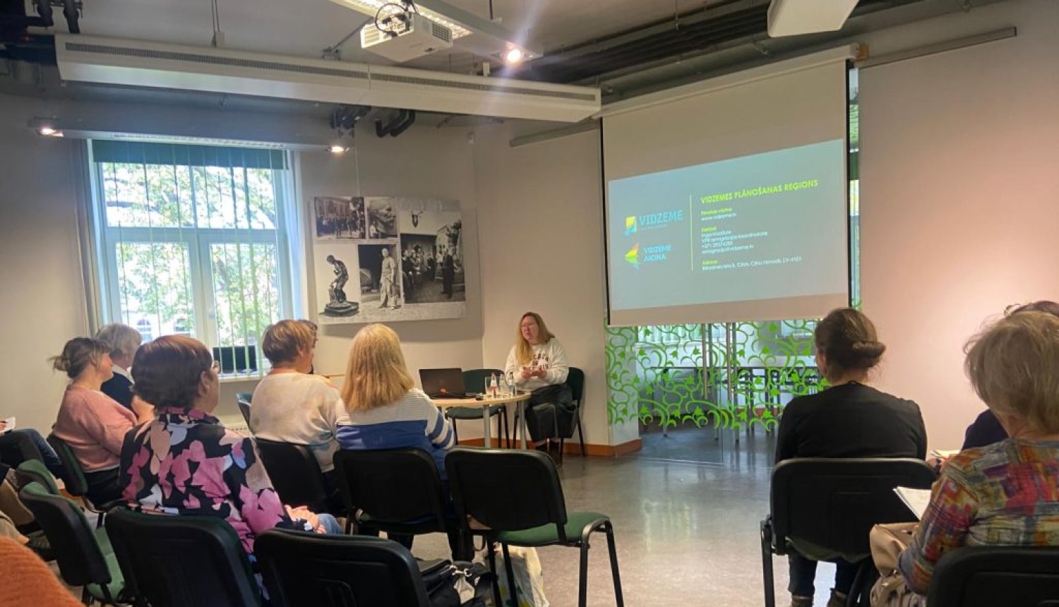 Cēsu Centrālās bibliotēkas telpa ar prezentāciju ekrānu un klausītājiem - Vidzemes bilbiotekāriem.