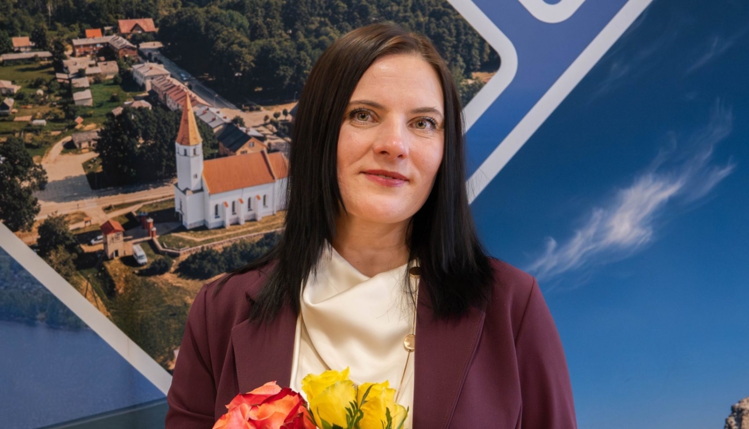 A young woman with dark brown hair stands holding yellow and pink roses, with a church visible in the background.