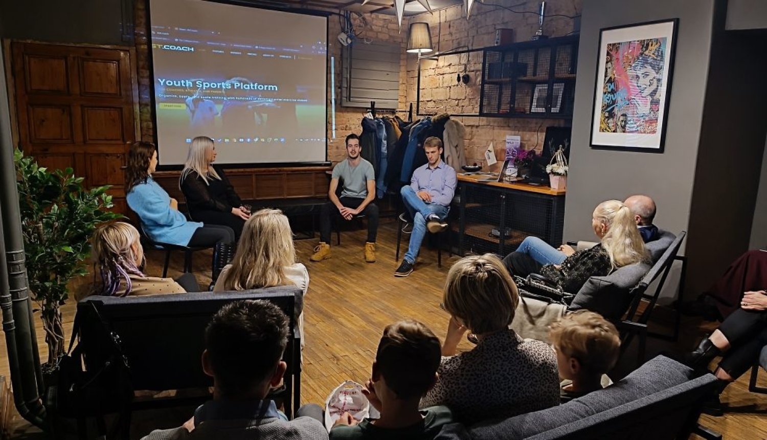 Pasākuma dalībnieki sēž un klausās remigrantu pieredzes stāstus trešajā “Remigrantu stāstu pēcpusdienā” kafejnīcā “Tērbata” Valmierā.