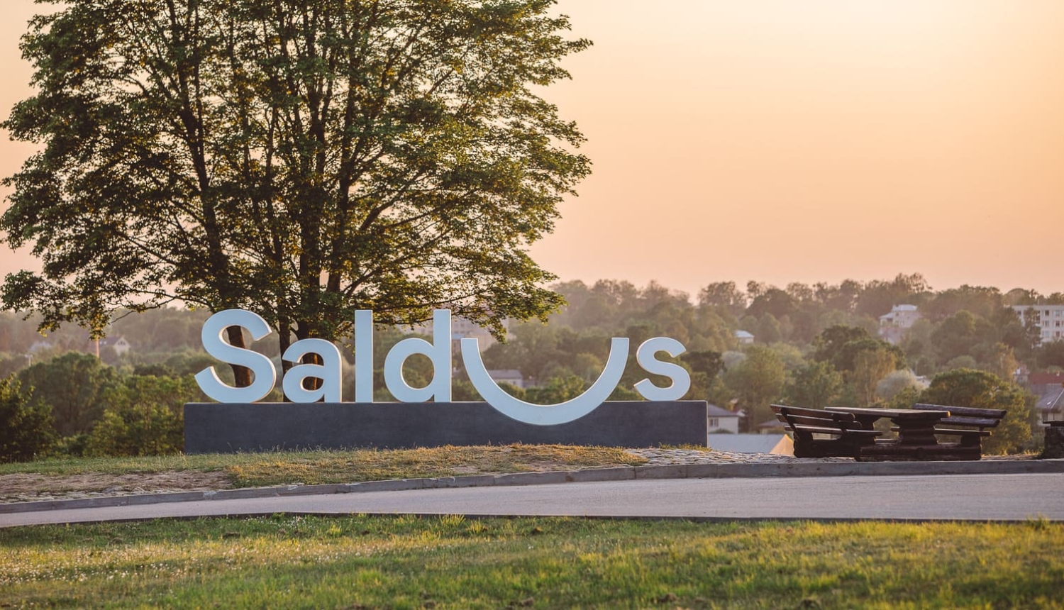 Ainava ar baltiem Saldus logo burtiem uz paaugstinājuma.