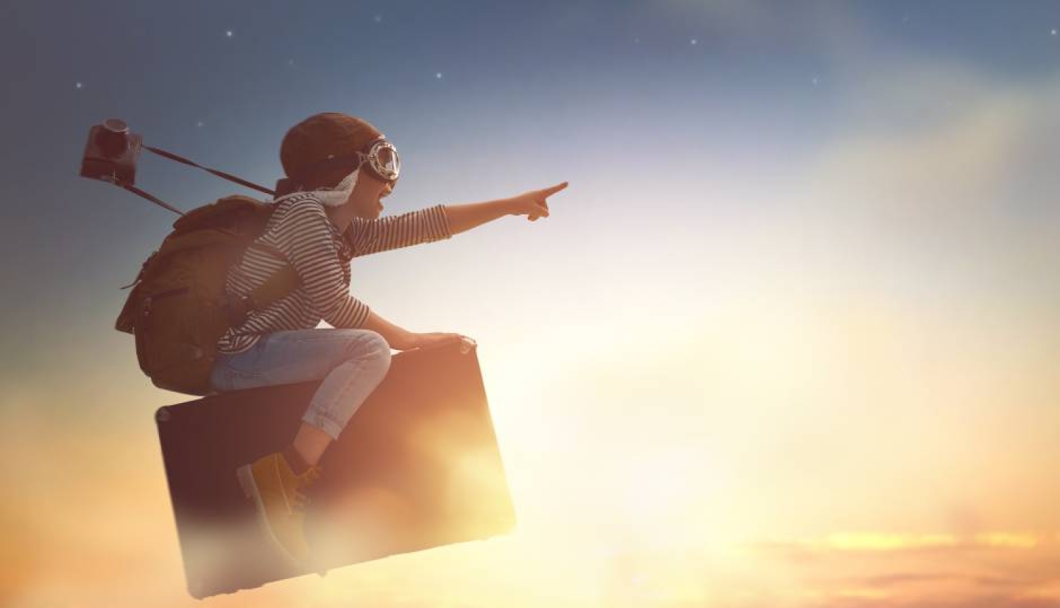 Cilvēks aviatora cepurē un brillēs ar mugursomu plecos lido uz ceļojumu kofera saulrieta debesu fonā un ar izstieptu rādītājpirkstu rāda uz priekšu.