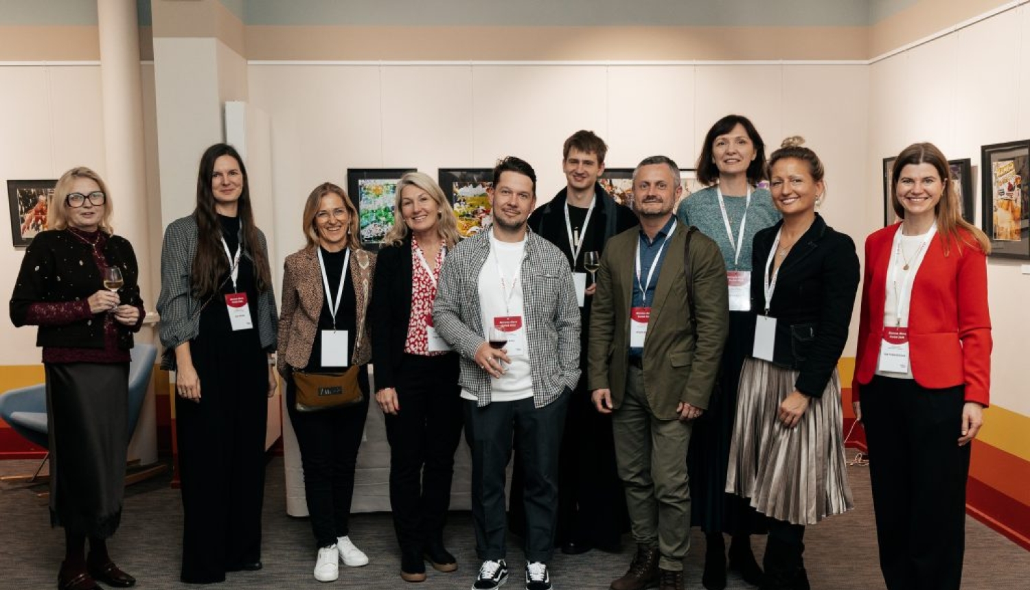 Desmit pasākuma "Biznesa diena Parīzē 2025" dalībnieki ar gleznām fonā.