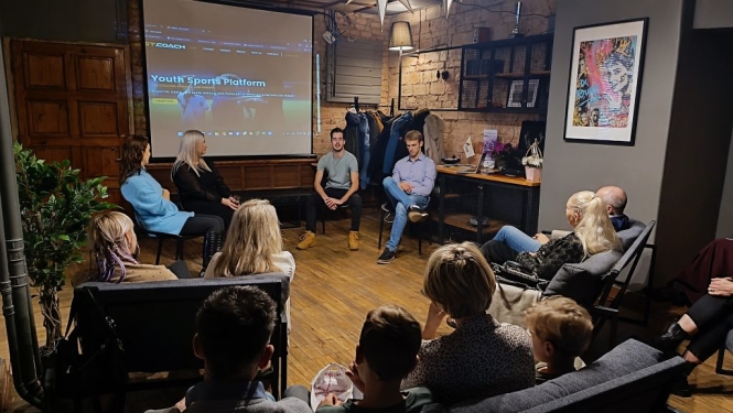 Pasākuma dalībnieki sēž un klausās remigrantu pieredzes stāstus trešajā “Remigrantu stāstu pēcpusdienā” kafejnīcā “Tērbata” Valmierā.